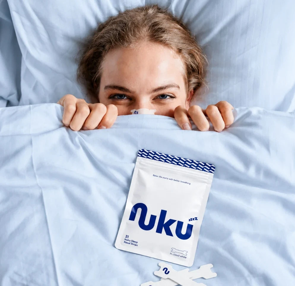 Woman under a duvet wearing a Nuku nasal strip, with a Nuku pack